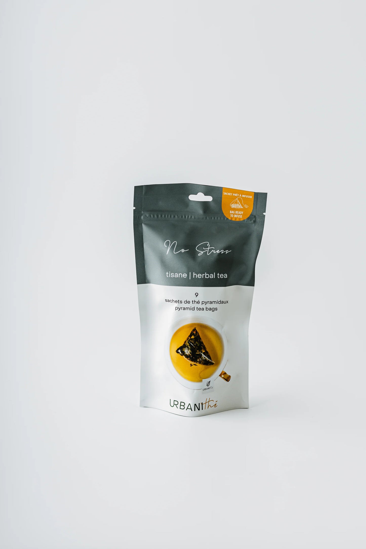 Tasse blanche à anse et soucoupe dorées avec sachet No Stress Urbanithé infusant, enveloppe individuelle bleue No Stress posée devant