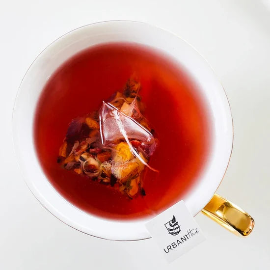 Sachet pyramidal Urbanithé infusant dans une tasse élégante à anse dorée — tisane Belle Framboise rouge profond vue du dessus