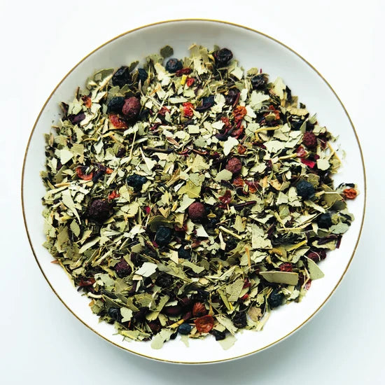 Vue de dessus du mélange sec Antidote Quatre Saisons Urbanithé — feuilles d’eucalyptus, myrtilles séchées, groseilles, thé vert et thym dans assiette blanche à rebord doré
