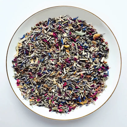 Vue de dessus du mélange sec Bleu de Fleurs Urbanithé — lavande bleue, citronnelle, centaurée bleue et pétales de rose dans assiette blanche à rebord doré