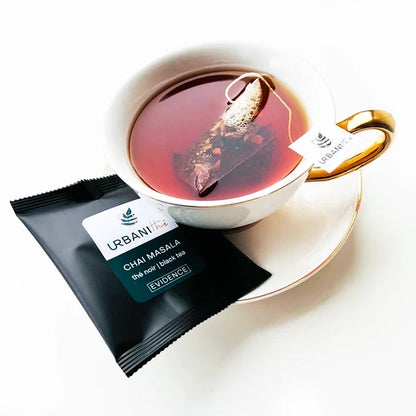 Tasse blanche à anse et soucoupe dorées avec sachet pyramidal Chai Masala Urbanithé infusant, enveloppe individuelle noire Chai Masala Evidence posée devant, fond blanc