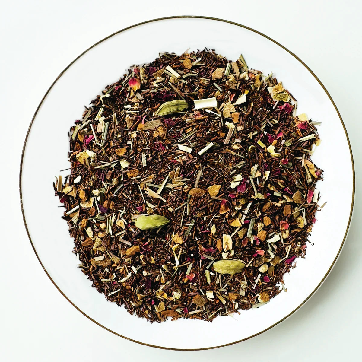 Vue de dessus du mélange sec Citron Exotique Urbanithé — rooibos, pétales de rose, citronnelle et épices dans assiette blanche à rebord doré