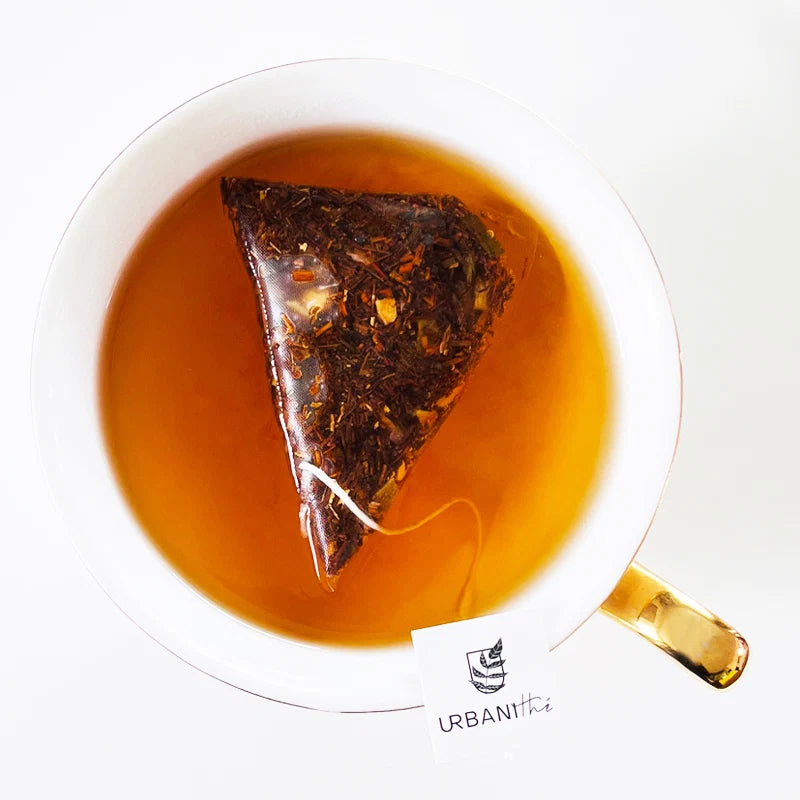 Vue de dessus d’une tasse blanche à anse dorée avec sachet pyramidal Citron Exotique Urbanithé infusant dans liquide ambré doré