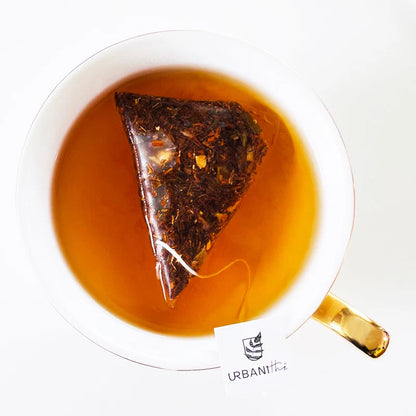 Vue de dessus d’une tasse blanche à anse dorée avec sachet pyramidal Citron Exotique Urbanithé infusant dans liquide ambré doré