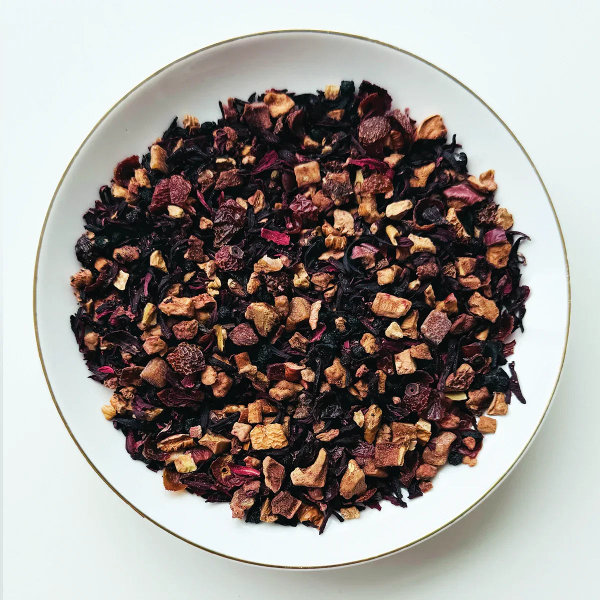 Vue de dessus du mélange sec Délice Fruité Urbanithé dans un bol blanc à rebord doré — hibiscus, fraise et fruits séchés colorés