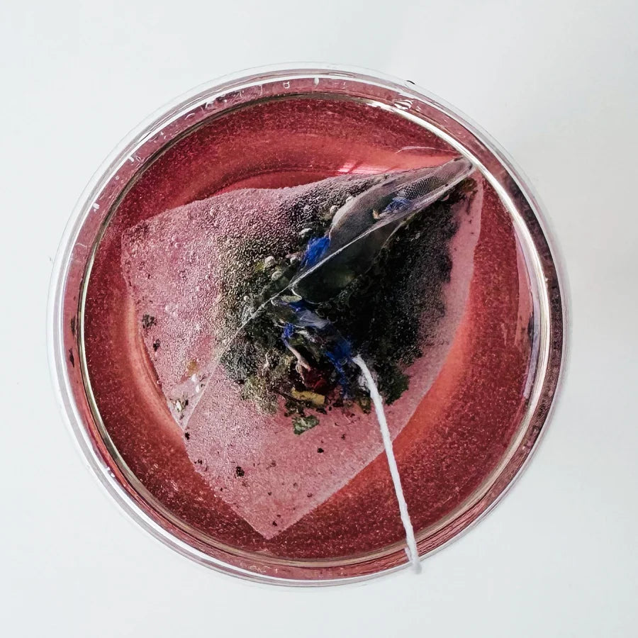 Vue de dessus d'un verre rond avec sachet pyramidal Éclat Divin Urbanithé infusant dans liquide rose-rouge profond