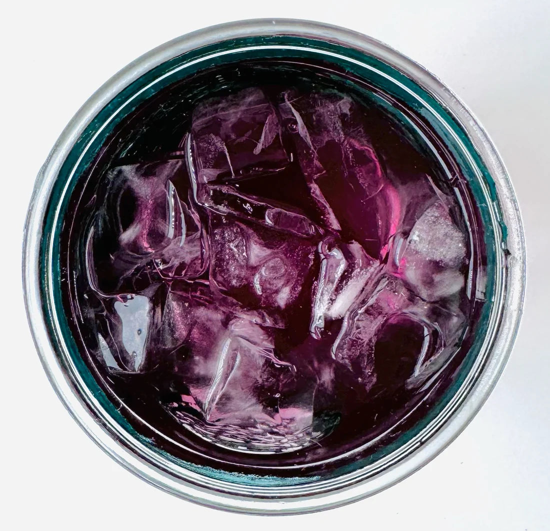 Vue de dessus d’un verre mason glacé contenant l’infusion à froid Elixir Bleu Urbanithé — liquide violet profond avec glaçons