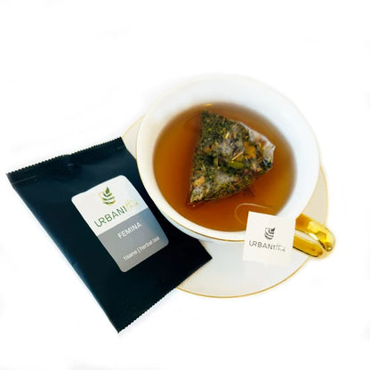 Tasse blanche à anse et soucoupe dorées avec sachet pyramidal Femina Urbanithé infusant dans liquide ambré, enveloppe individuelle noire Femina posée devant, fond blanc