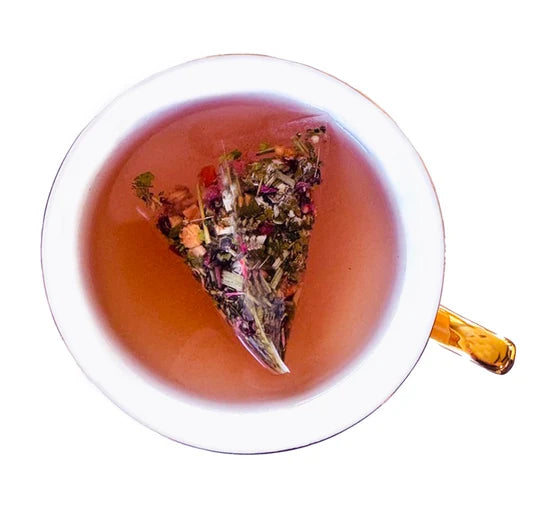 Vue de dessus d'une tasse en verre avec sachet pyramidal Femina Urbanithé infusant dans liquide rouge rosé, fond blanc