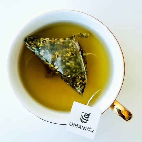 Vue de dessus d’une tasse blanche à anse dorée avec sachet pyramidal Focus Urbanithé maté matcha infusant dans liquide vert doré, fond blanc