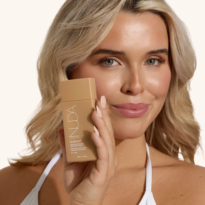 Femme blonde tenant l'écran solaire minéral SolarGlow NUDA 50 ml — sérum solaire FPS 30 léger et lumineux — Spa Santé Le Nénuphar
