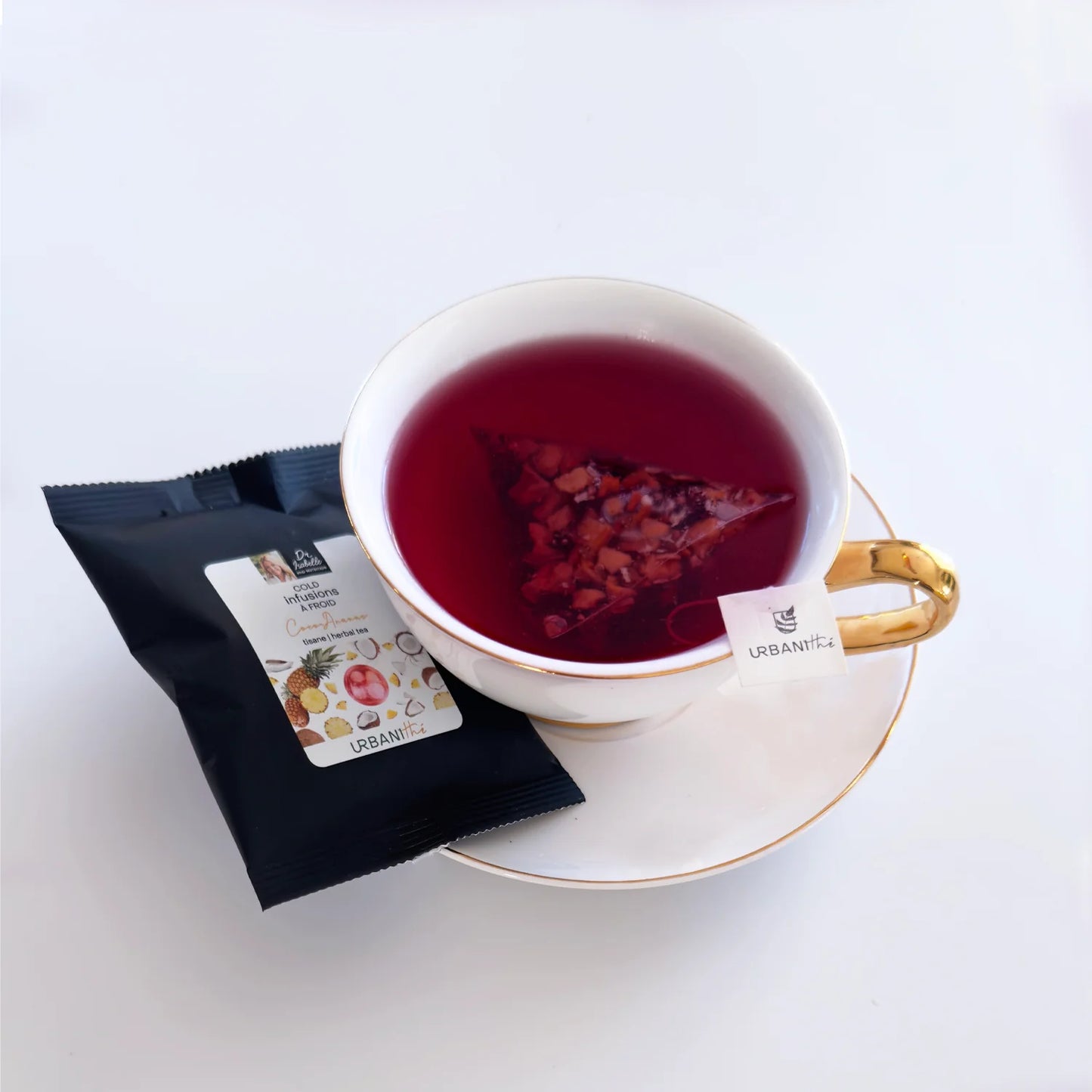 Emballage individuel Coco-Ananas Urbanithé avec sachet pyramidal infusant dans une tasse blanche à anse dorée sur soucoupe