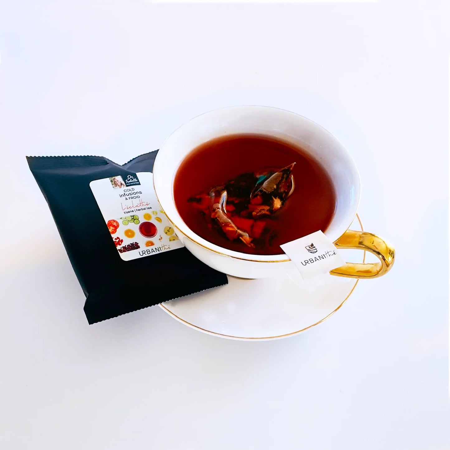Sachet pyramidal L’Éclathé Urbanithé infusant dans une tasse blanche à anse dorée avec emballage individuel noir