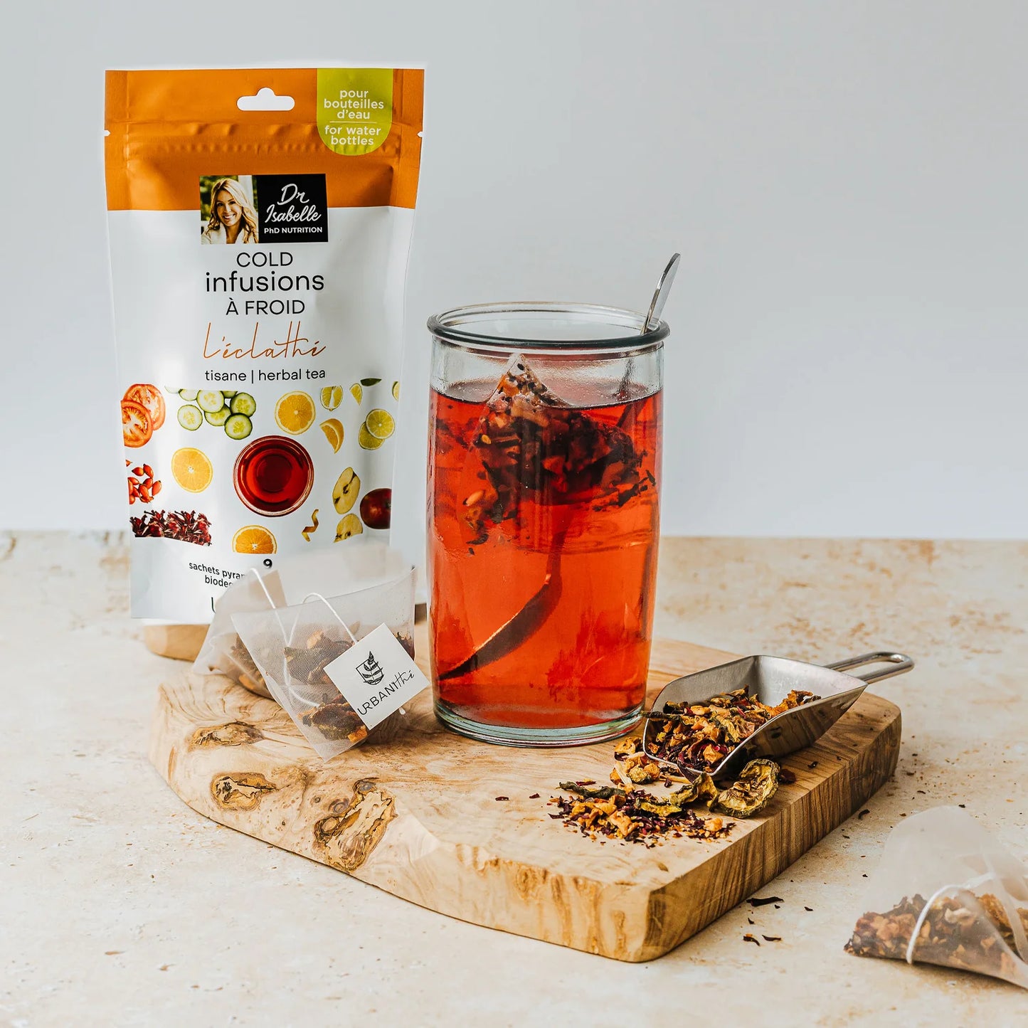 Infusion L’Éclathé Urbanithé infusant dans un verre haut sur planche de bois avec sachet pyramidal et mélange de plantes séchées