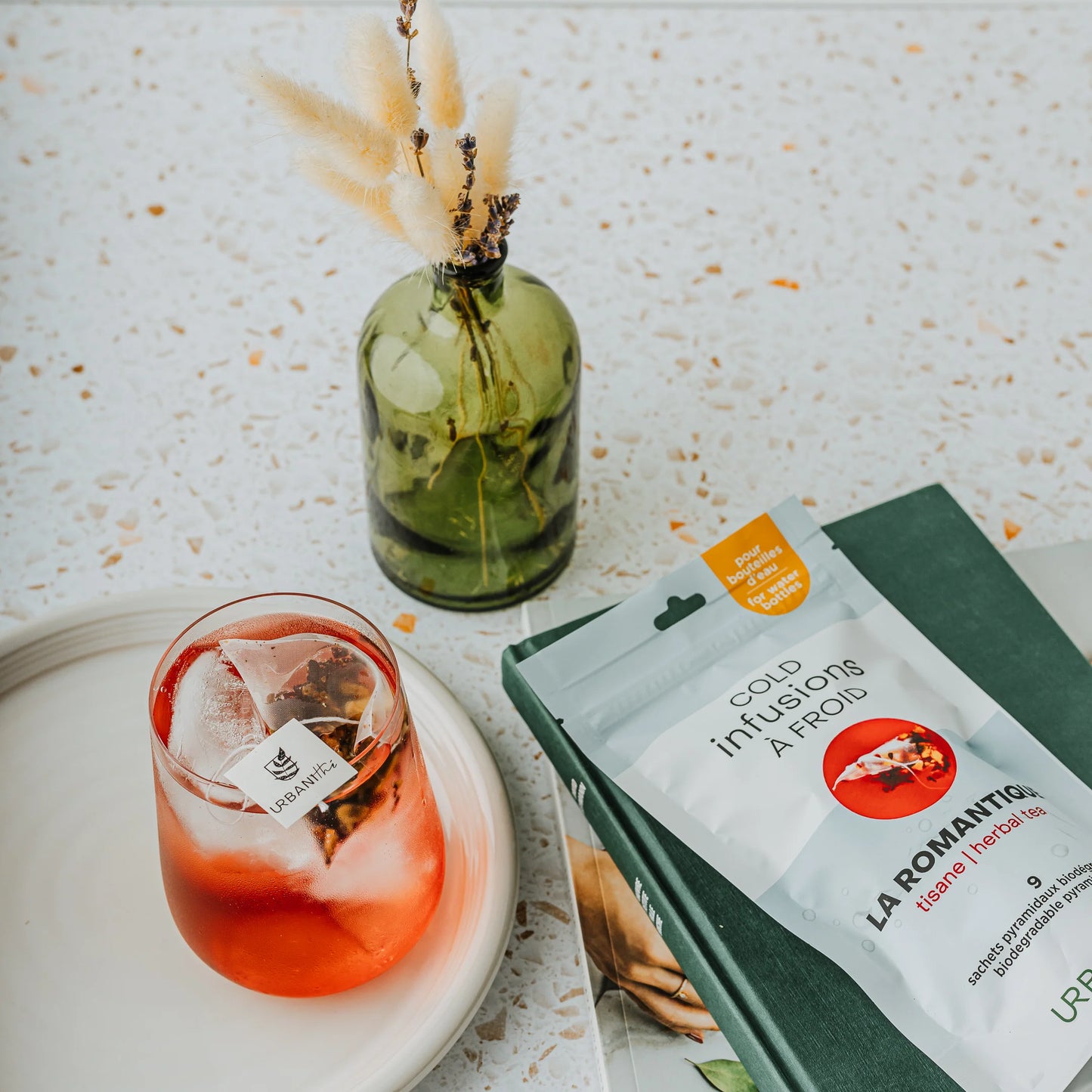 Tasse blanche à anse dorée avec sachet pyramidal La Romantique Urbanithé infusant — liquide rouge profond, emballage noir rose à côté