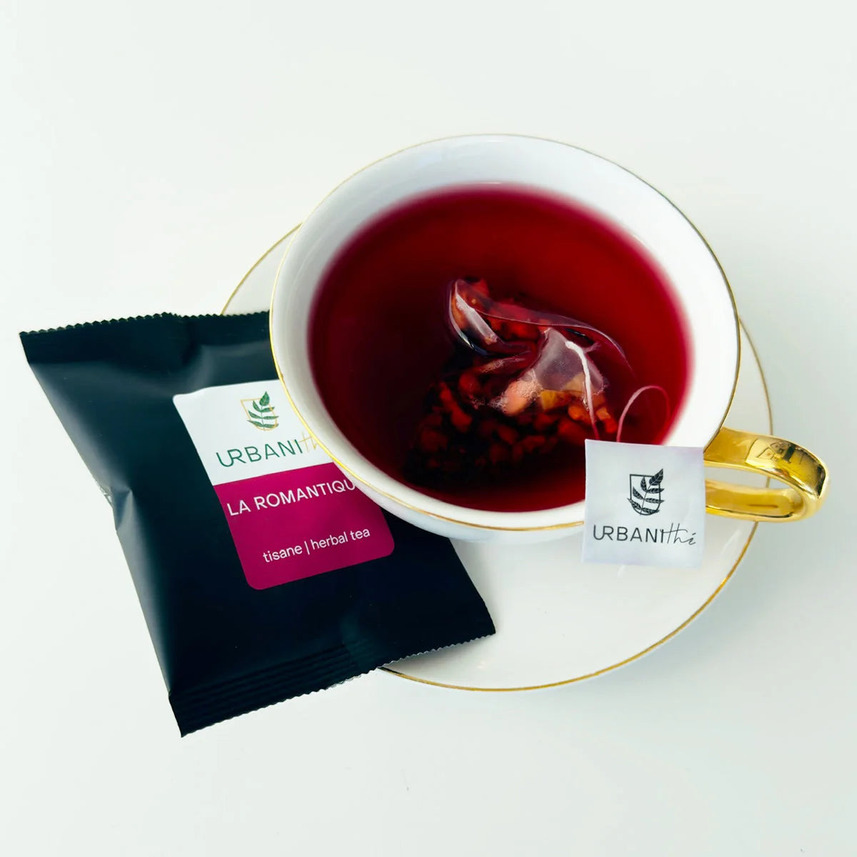 Emballage individuel sachet La Romantique Urbanithé avec tasse blanche à anse dorée sur soucoupe, fond blanc épuré