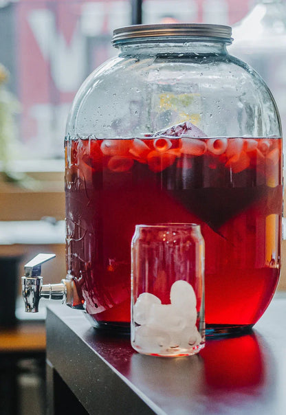 Grand thermos en verre rempli de tisane La Romantique Urbanithé rouge vif avec petits fruits — verre glacé à côté pour service