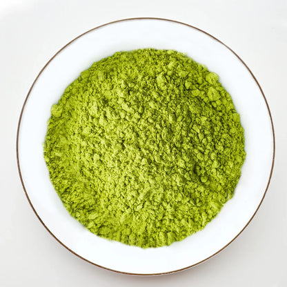 Vue de dessus poudre de matcha vert vif Urbanithé saveur naturelle dans assiette blanche bordée or, sans fruit, fond blanc