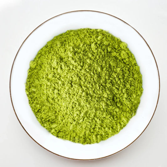 Vue de dessus poudre de matcha vert vif Urbanithé saveur naturelle dans assiette blanche bordée or, sans fruit, fond blanc
