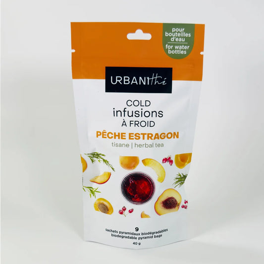 Emballage Pêche Estragon Urbanithé Cold Infusions À Froid 40g posé à côté d'un verre cylindrique transparent avec infusion rouge glacée et sachet pyramidal