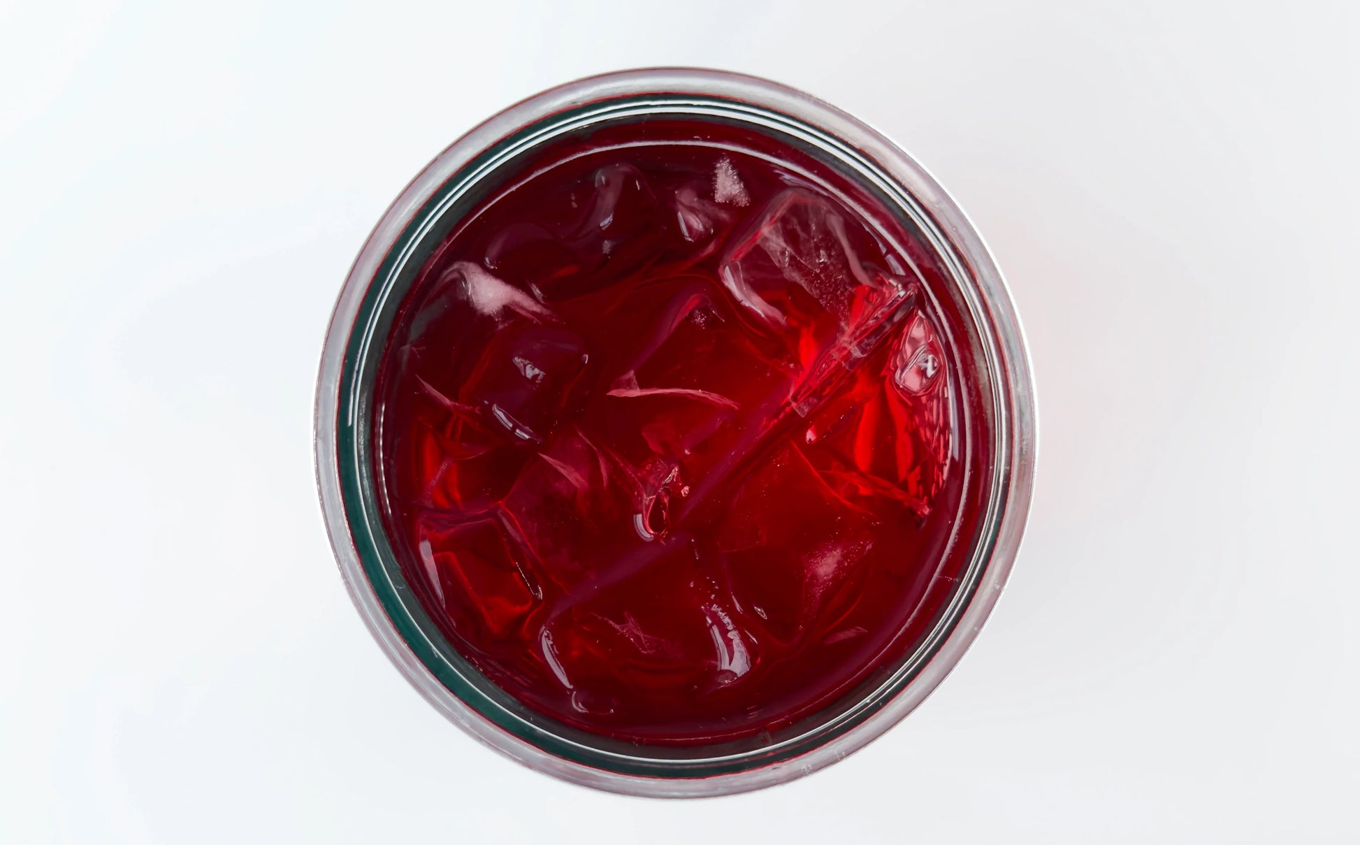 Vue de dessus d'un verre mason rond avec infusion à froid Pêche Estragon Urbanithé — liquide rouge profond avec glaçons, fond blanc