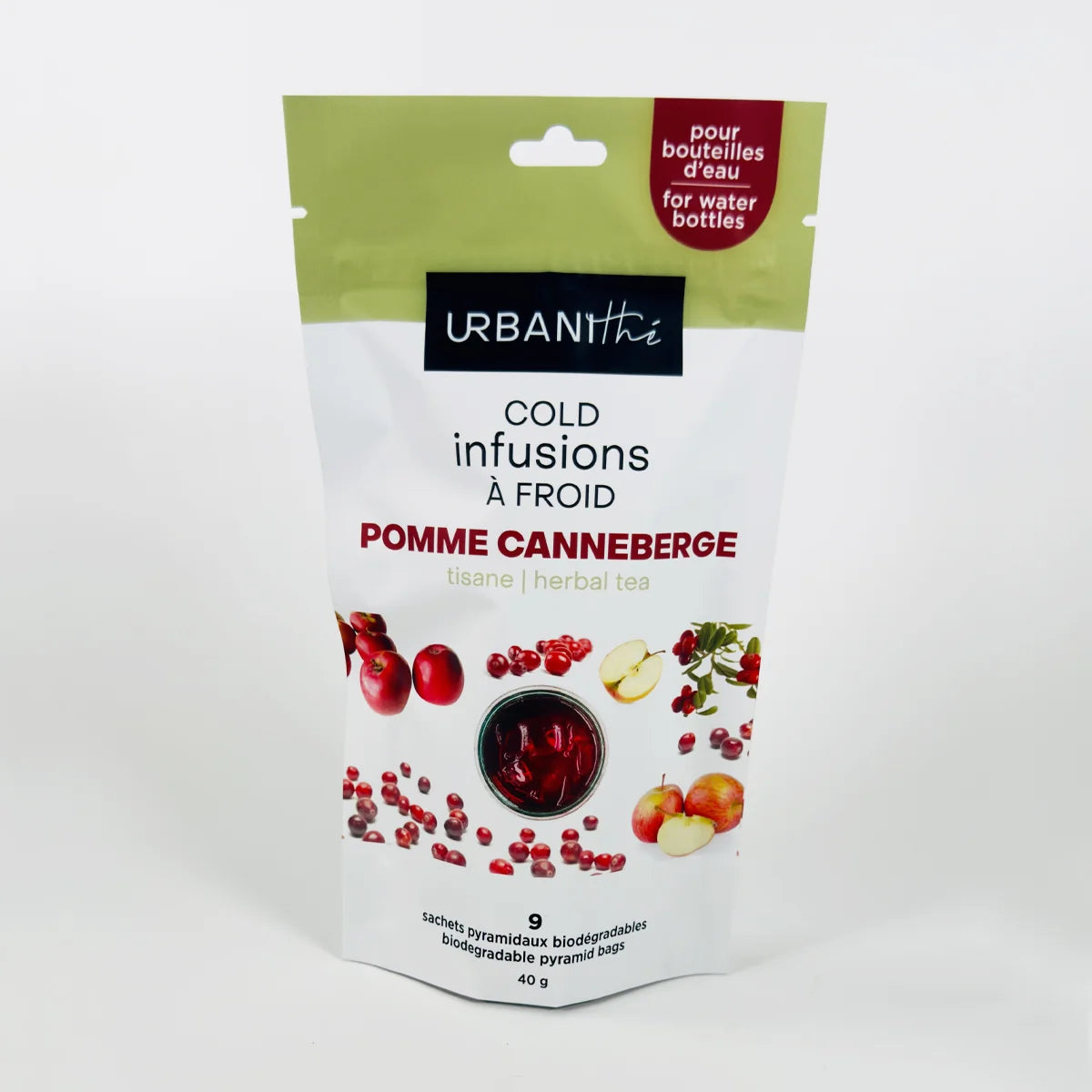 Vue de dessus d'une tasse blanche à anse dorée avec sachet pyramidal Pomme Canneberge Urbanithé infusant dans liquide rouge profond, fond blanc