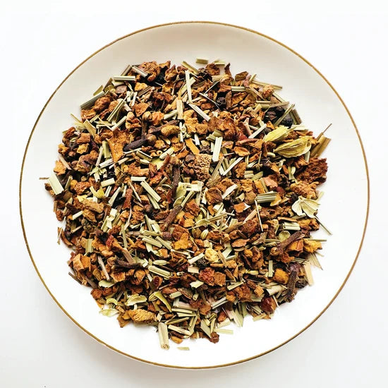Vue de dessus du mélange sec Pomme Épicée Urbanithé — pomme séchée, cannelle, gingembre, citronnelle, cardamome et clou de girofle dans assiette blanche à rebord doré