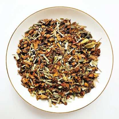 Vue de dessus du mélange sec Pomme Épicée Urbanithé — pomme séchée, cannelle, gingembre, citronnelle, cardamome et clou de girofle dans assiette blanche à rebord doré
