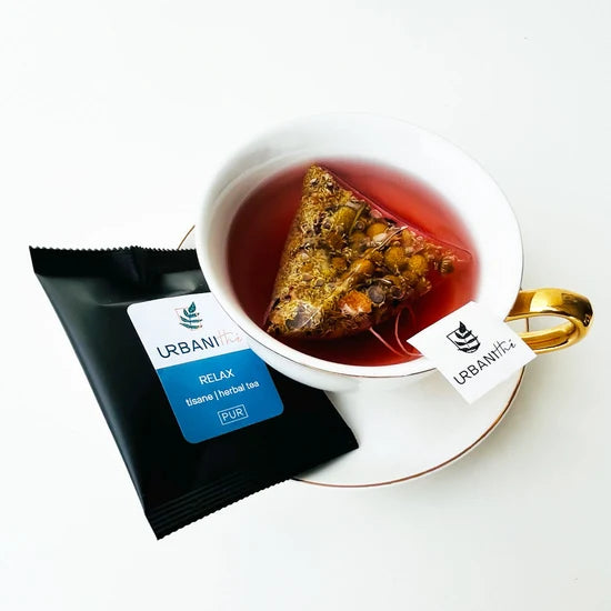 Vue de dessus du mélange sec Relax Urbanithé — camomille, pomme, hibiscus, carthame, tournesol dans assiette blanche à rebord doré
