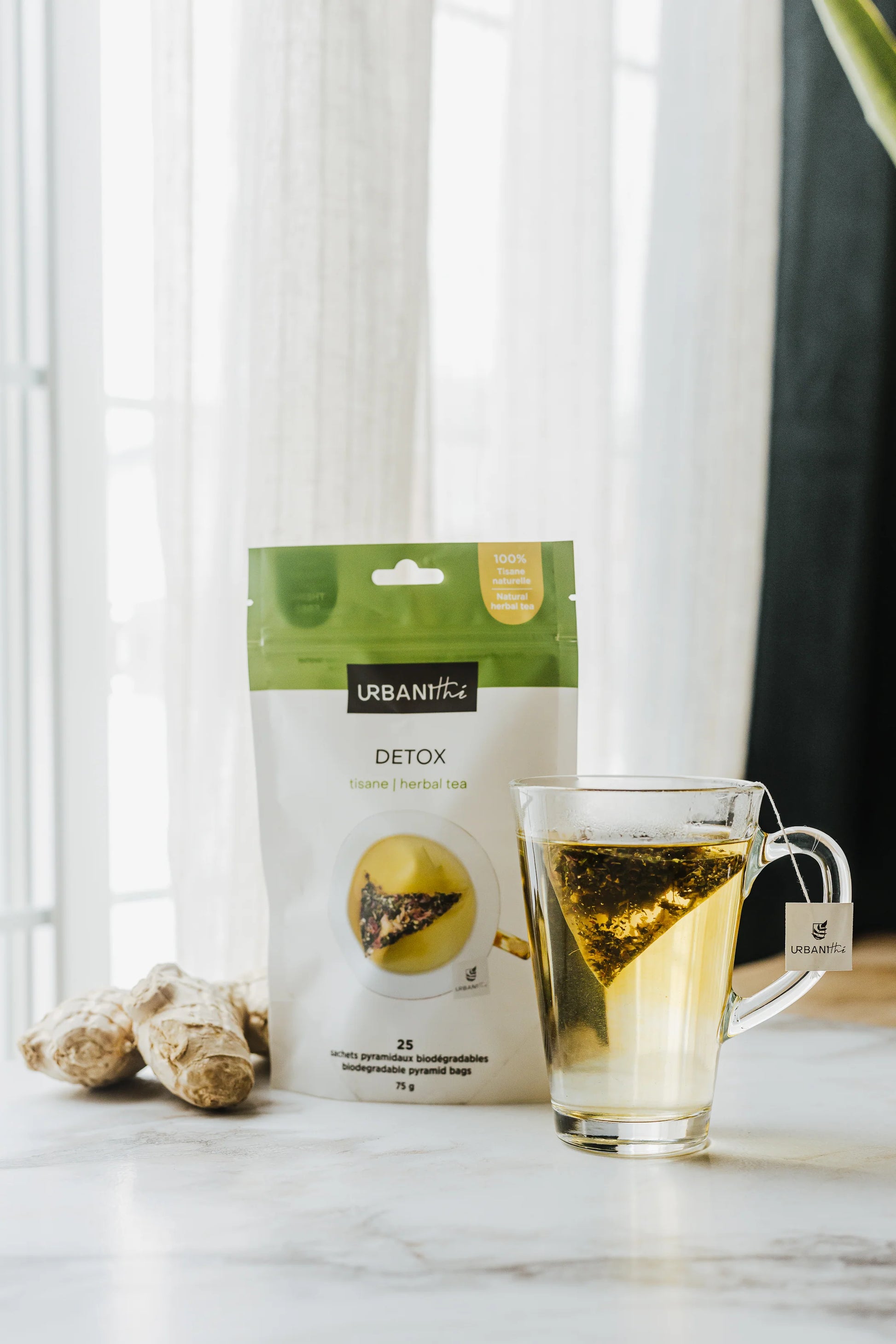 Emballage Detox Urbanithé 25 sachets 75g posé près d’une tasse en verre avec sachet infusant et gingembre frais