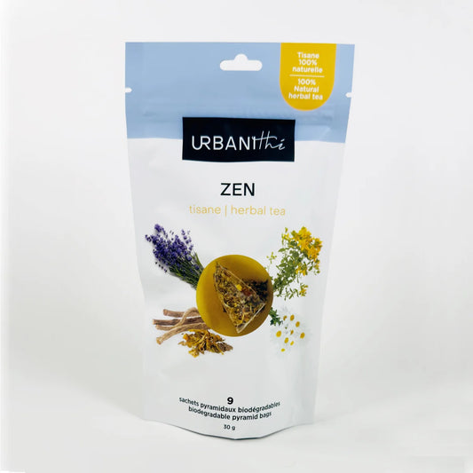 Vue de dessus d'une tasse blanche à anse dorée avec sachet pyramidal Zen Urbanithé infusant dans liquide doré ambré, fond blanc